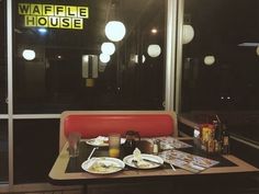 a table with food and drinks on it in front of a window that reads waffle house