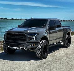 a large gray truck parked on top of a dirt road next to the ocean in front of a blue sky