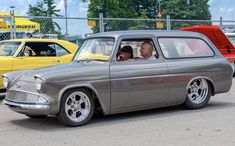 an old car is parked in a parking lot with other cars and people behind it