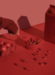 a red table topped with lots of food and a person reaching for something in a bowl