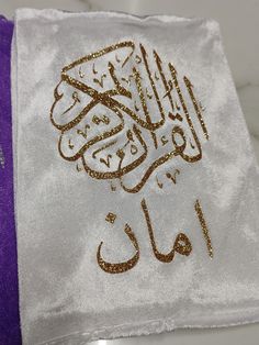 a white towel with gold arabic writing on it and a purple bag in the background