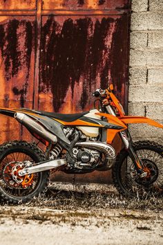 an orange and black dirt bike parked in front of a rusted building with the door open