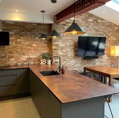 a kitchen with an island and television mounted to the brick wall above it, along with two bar stools