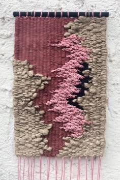 a woven wall hanging with pink flowers and leaves on the side of a white building