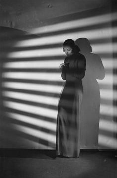 a woman standing in front of a window next to a shadow cast on the wall