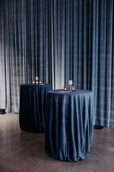 two round tables with blue cloth on them in front of a curtained wall and floor