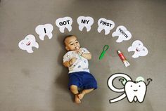 a baby laying on the floor next to toothbrushes and paper cutouts that say i got my first tooth
