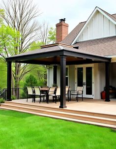 a covered patio with table and chairs in front of a white house surrounded by green grass