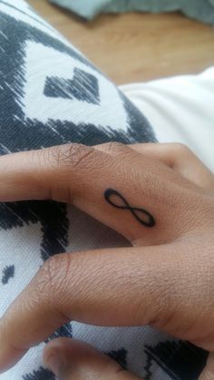 a person's hand with a tattoo on their left thumb and an infinite symbol on the middle finger