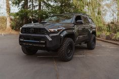 a black toyota truck parked in a parking lot next to some trees and bushes on the other side of the road