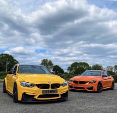 two orange cars parked next to each other in a parking lot with cloudy skies behind them