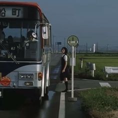 a woman standing in front of a bus on the side of the road next to a field