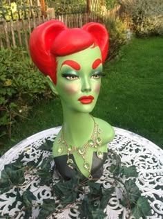 a statue of a woman with red hair and green makeup on a white table outside
