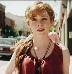 a woman with long hair standing in front of a building on a city street smiling at the camera