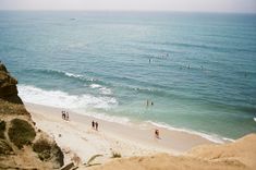 people are walking on the beach near the water's edge as swimmers swim in the ocean