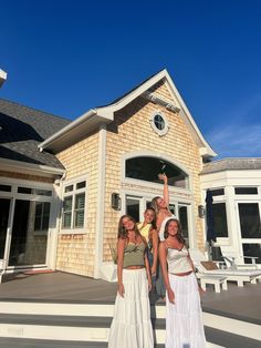 three girls standing in front of a house with their arms up and one girl raising her hand