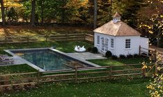a small white house sitting on top of a lush green field next to a swimming pool