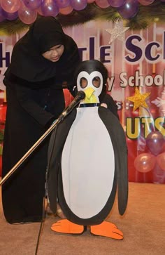 a woman in a black hijab is standing next to a penguin with a broom