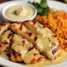 a white plate topped with chicken covered in gravy next to rice and veggies