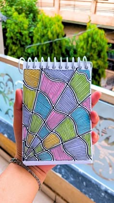 a hand holding a small notebook with colorful designs on it