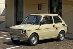 an old car is parked in front of a small building on a cobblestone street