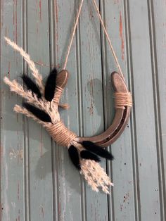 a wreath with feathers hanging on the side of a wooden door or wall, decorated with rope and jute