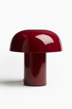 a red table lamp sitting on top of a white floor next to a light bulb