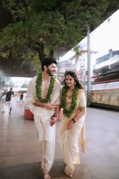a man and woman dressed in white are walking down the street with garlands around their necks