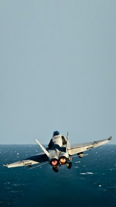 a fighter jet flying over the ocean on top of it's back legs and landing gear