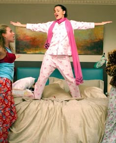 a woman standing on top of a bed with her arms outstretched in front of two other women