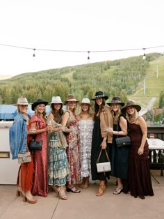 a group of women standing next to each other in dresses and hats on top of a roof