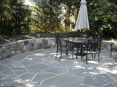 an outdoor table and chairs are set up on a stone patio with an umbrella over it