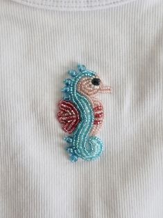 a close up of a sea horse embroidered on a white shirt with blue and red beads