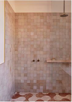 a bathroom with a tiled wall and floor, shower head and shelf in the corner