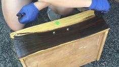 a person with blue gloves on kneeling down next to a wooden box