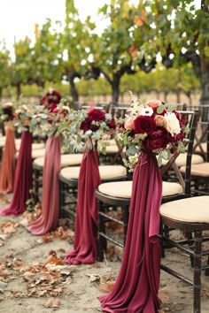 a row of chairs with red sashes and bouquets on them in an outdoor setting
