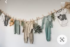 baby clothes hanging on a clothes line with teddy bears and plants next to them in front of a white wall