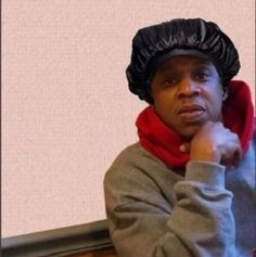 a man wearing a black hat and red scarf is sitting on a bench with his hand under his chin