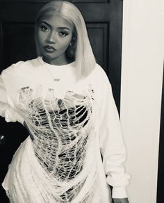 a woman with blonde hair wearing a white shirt and ripped skirt standing in front of a door