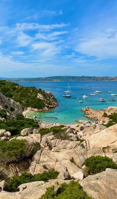 the beach is full of people and boats on it's sides, with rocks in the foreground