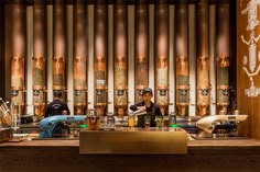 two men are behind the bar in front of some copper pipes and beer bottles on display