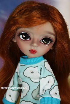 a close up of a doll with long red hair and big eyes wearing a blue sweater