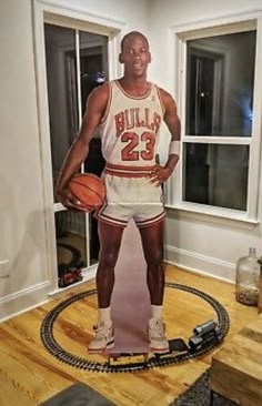 a man standing in front of a basketball on top of a wooden floor next to a window