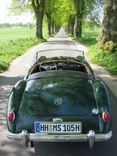 an old green convertible car parked on the side of a road in front of trees