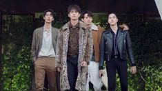 four men standing next to each other in front of some bushes and trees with one man wearing a leopard print coat