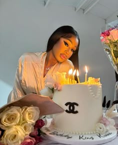 a woman sitting in front of a white cake with lit candles on it and flowers