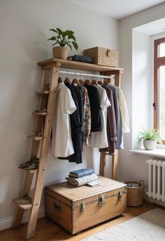 a wooden shelf with clothes hanging on it next to a window and an old suitcase