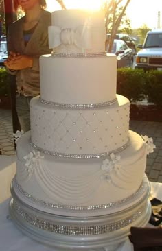 a large white wedding cake sitting on top of a table next to a woman standing behind it