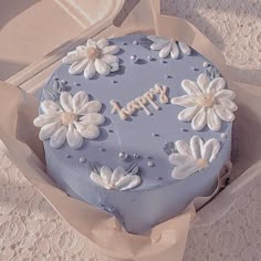 there is a blue cake with white flowers on it and the words happy written in frosting