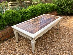 a coffee table sitting on top of a gravel ground next to bushes and shrubbery